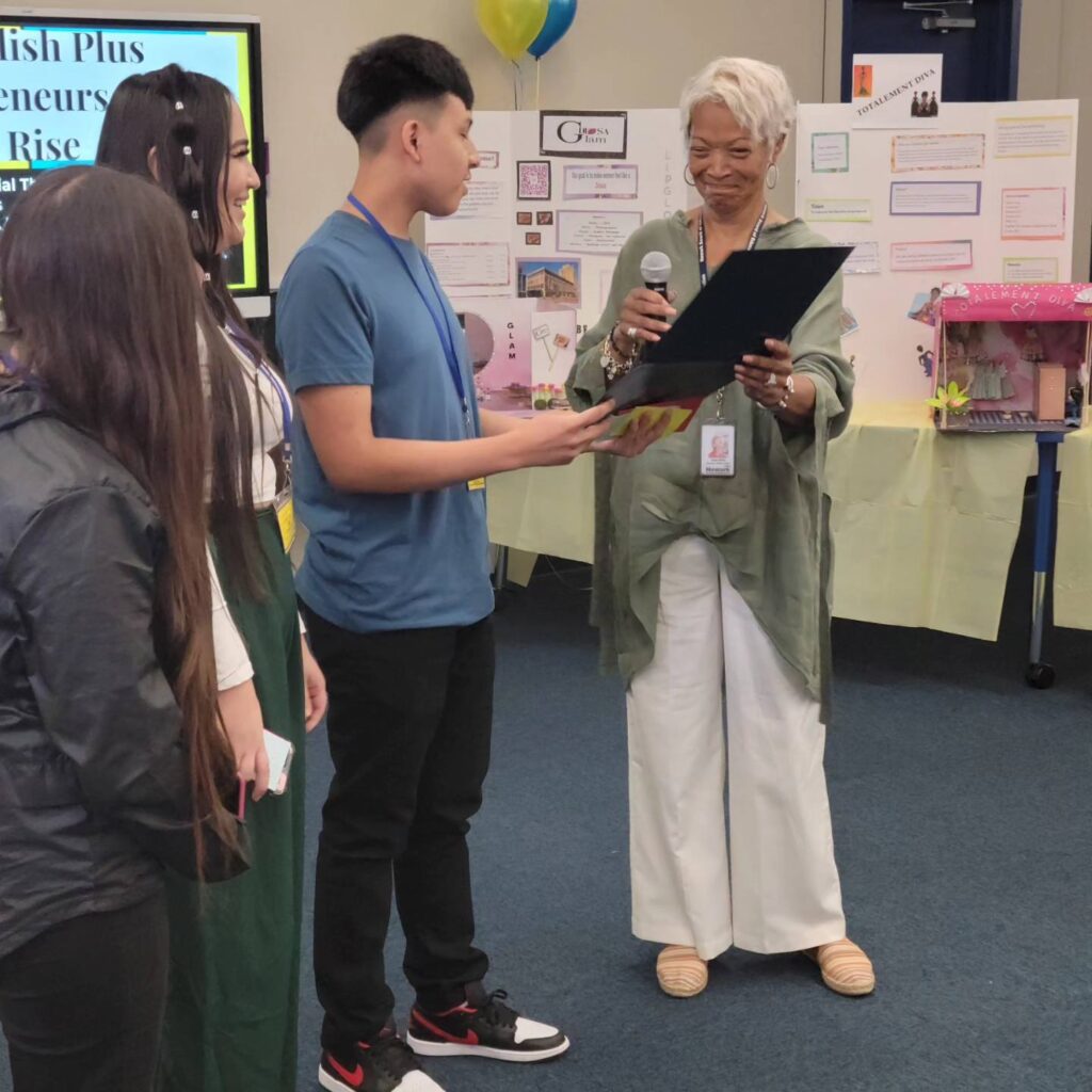 Sadia White, an Executive Mentor for The Newark Board of Education, presents students with a check for one hundred dollars to sustain their business